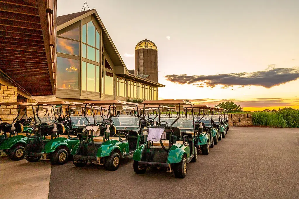 Golf carts lined up outside a clubhouse at sunset